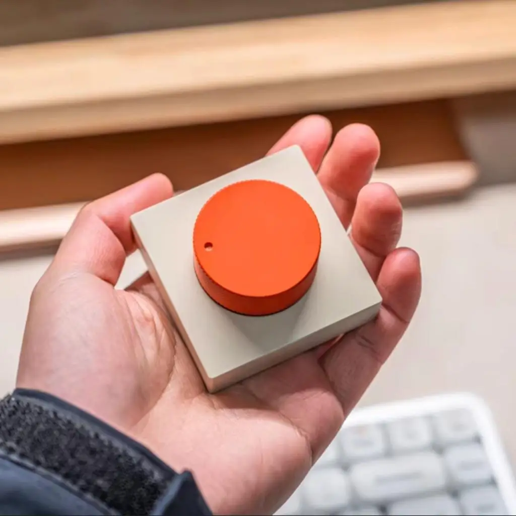 Programmable wireless knob with orange aluminum dial resting on a modern workspace